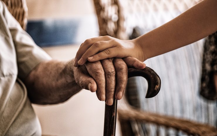 persona che mette la sua mano sopra a quella di un anziano seduto e con il bastone