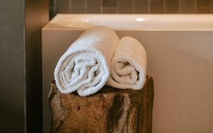 Asciugamani morbidi e bianchi arrotolati sopra a un tronco vicino la vasca